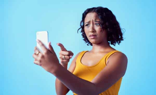 Social media, confused and phone app with a woman, smartphone and puzzled face about connection. Female having problems or trouble with mobile technology pointing against a blue studio background.