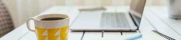 A cup of coffee sits next to a laptop on a digital marketer's desk.